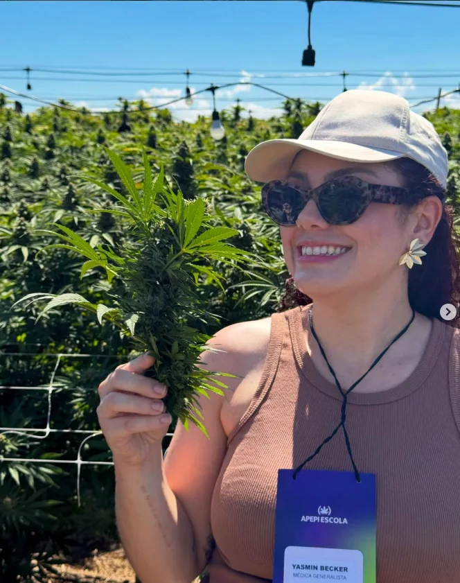 Publicação do Instagram: Dra. Yasmin Becker em visita a um cultivo de cannabis, segurando uma planta