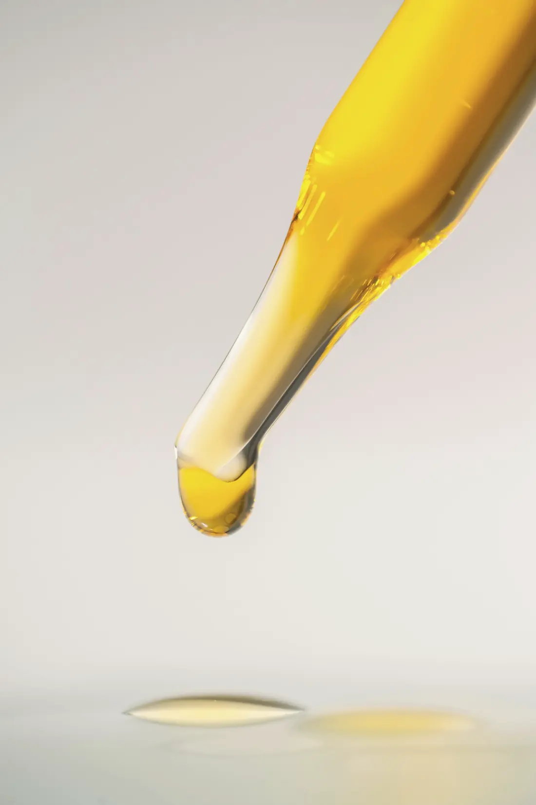 Gota de óleo dourado caindo da ponta de um conta-gotas
