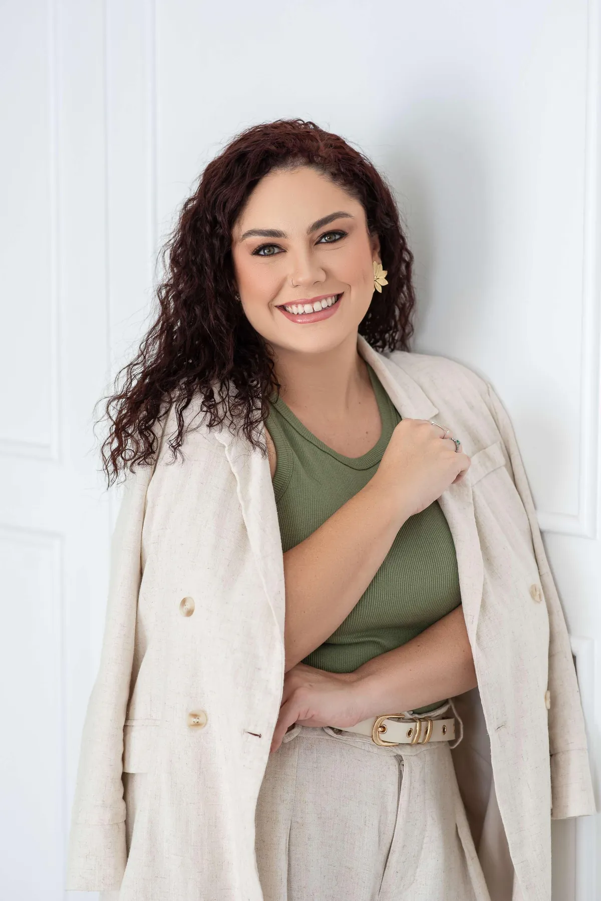 Dra. Yasmin Becker sorrindo, de blusa verde e blazer de linho, encostada numa parede clara